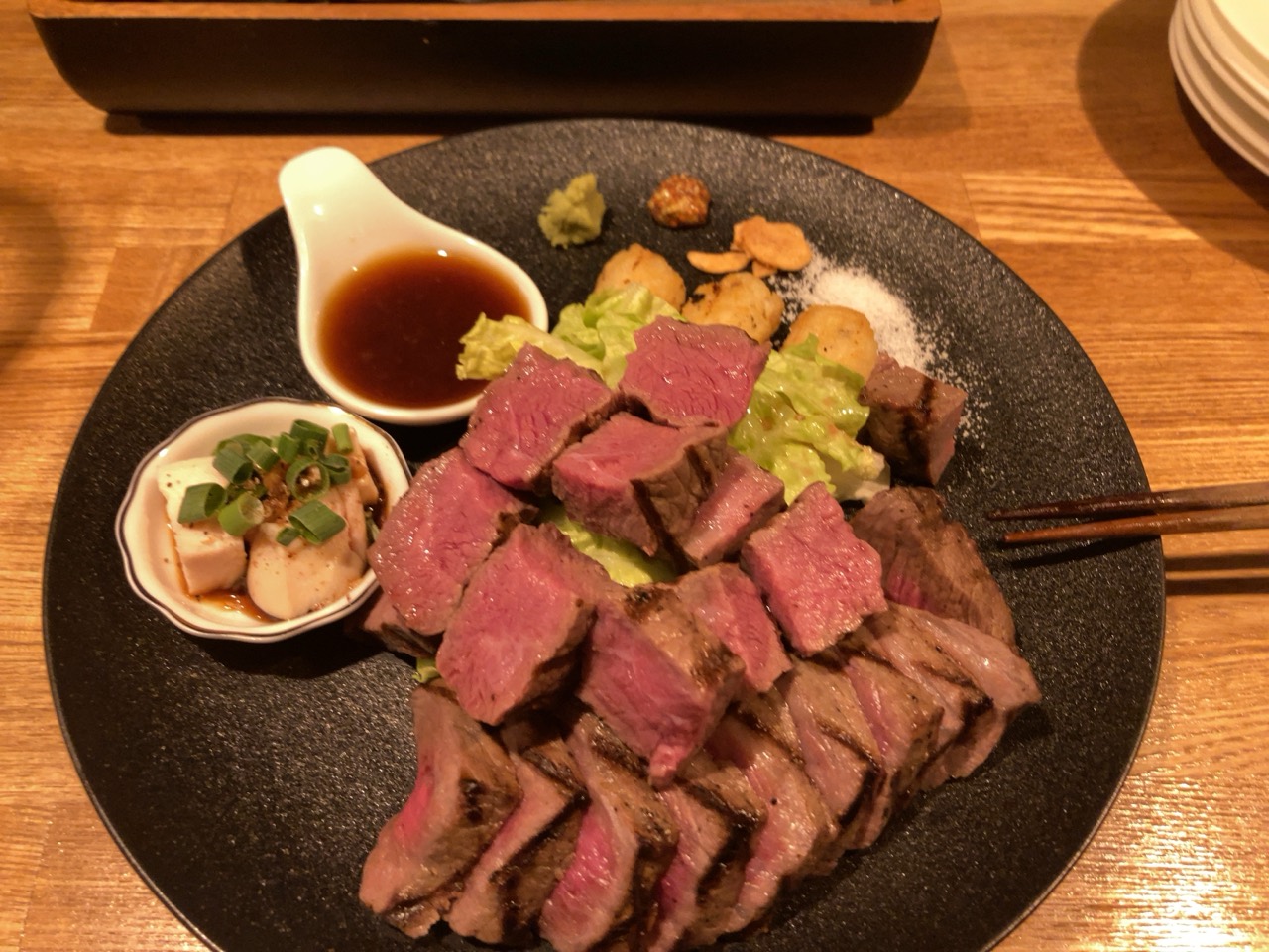 黒い皿に盛られた厚切りの肉料理と付け合わせ
