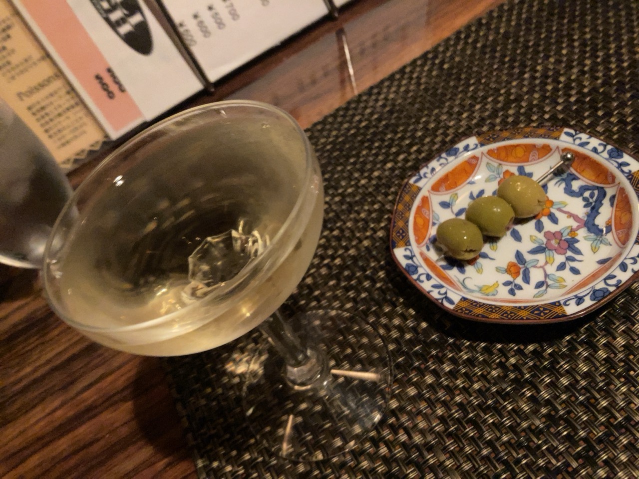 模様のある小皿のオリーブ3粒と、脚付きグラスに注がれたマティーニ