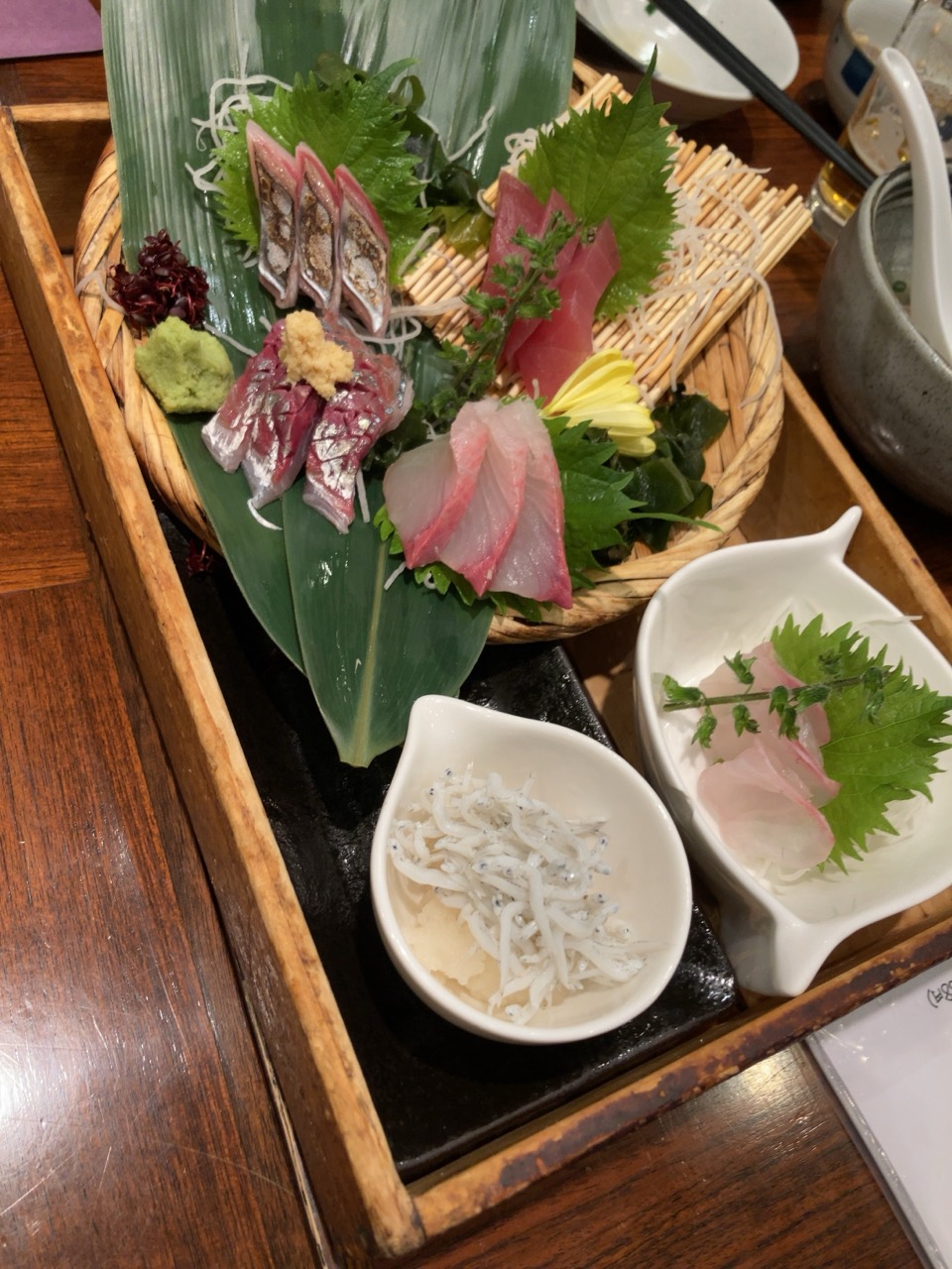 竹籠に並ぶ刺身の盛り合わせと小鉢