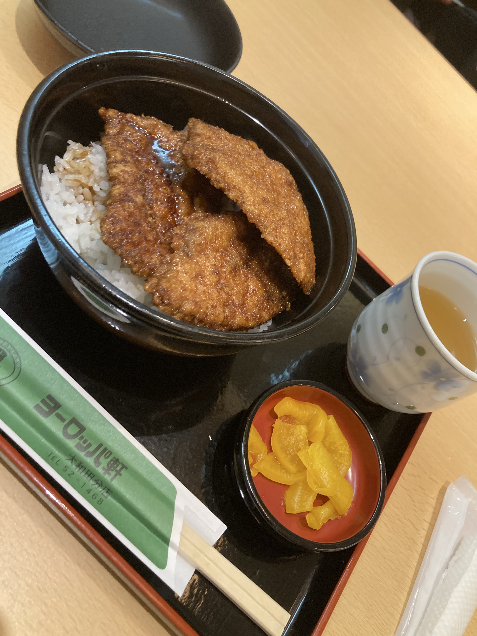 黒い丼に盛られたソースカツ丼と黄色い漬物